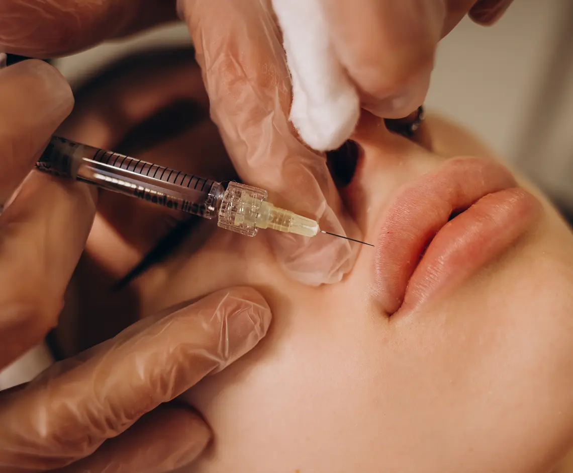Close up of hands of cosmetologist making botox injection in female lips. She is holding syringe