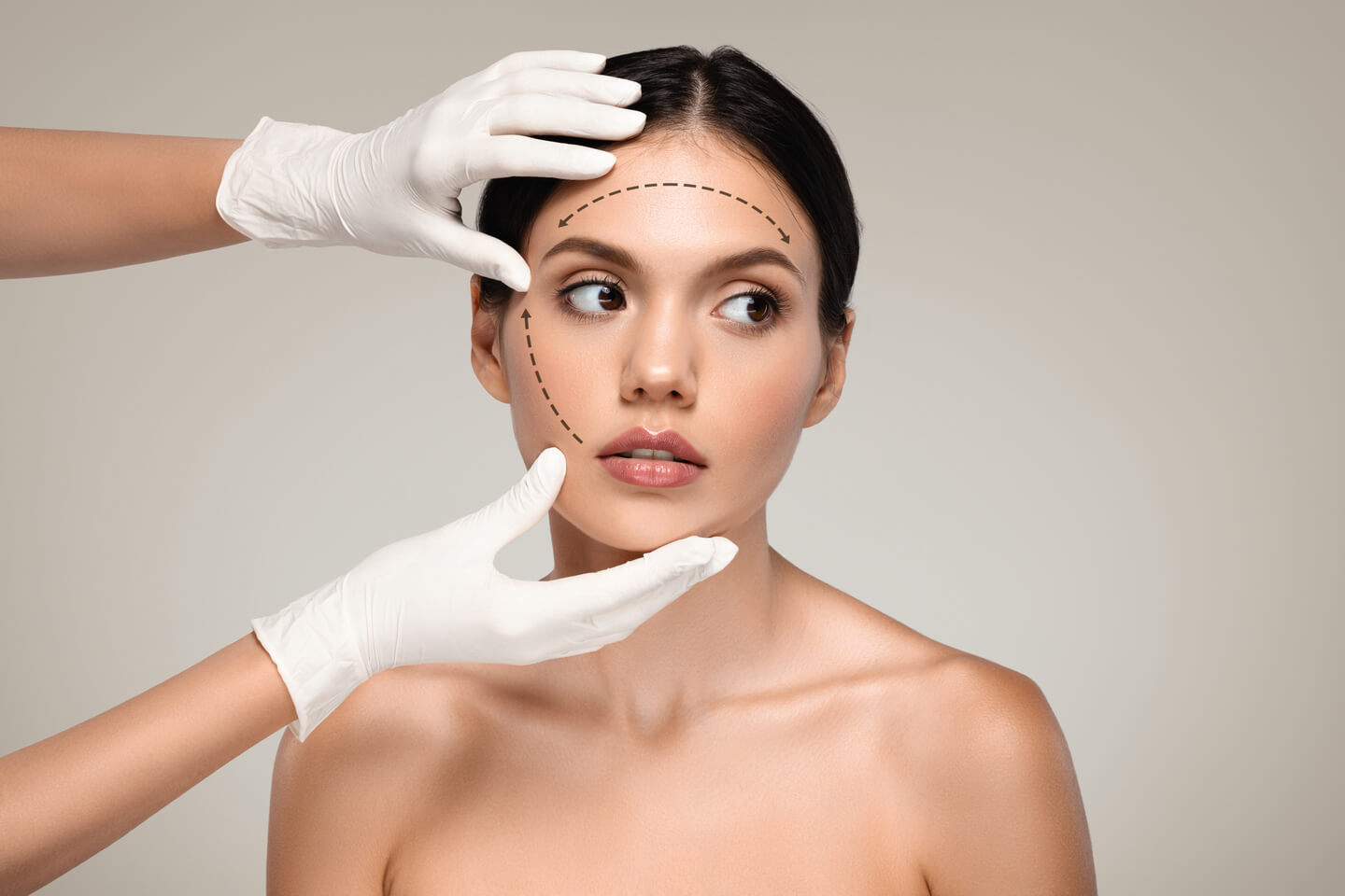 Hands of cosmetologist in gloves make exam to serious millennial european woman