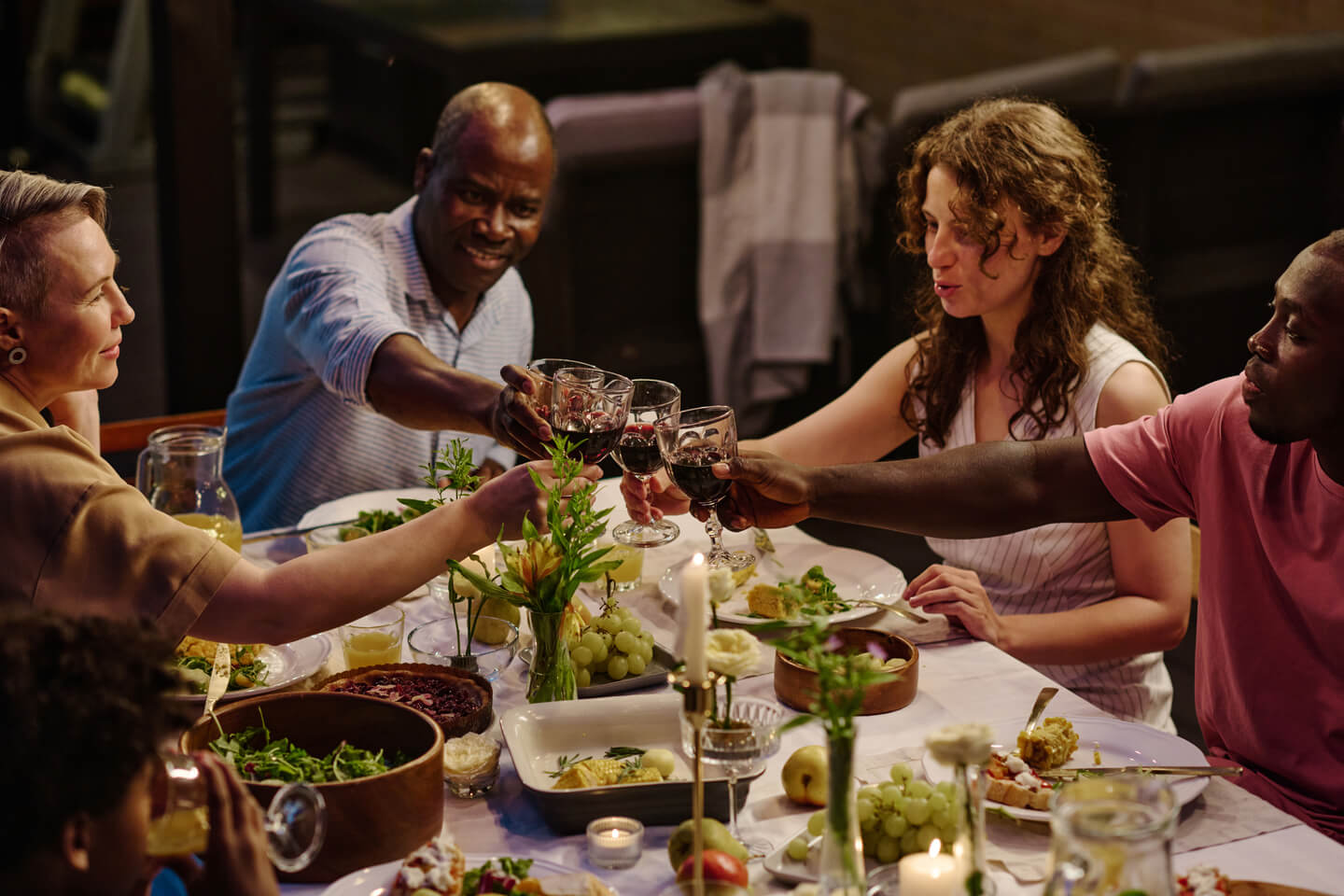 Intercultural family of five sitting by served table and toasting with red wine
