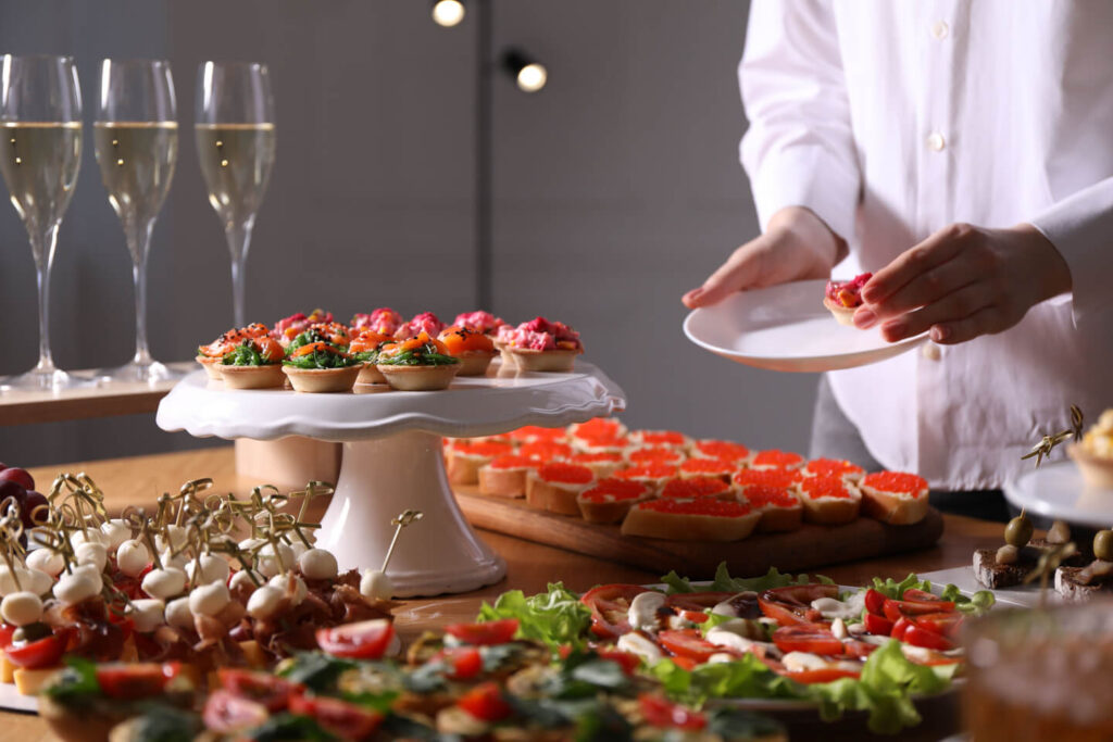 Buffet menu. Woman taking tasty tartlet from table, closeup