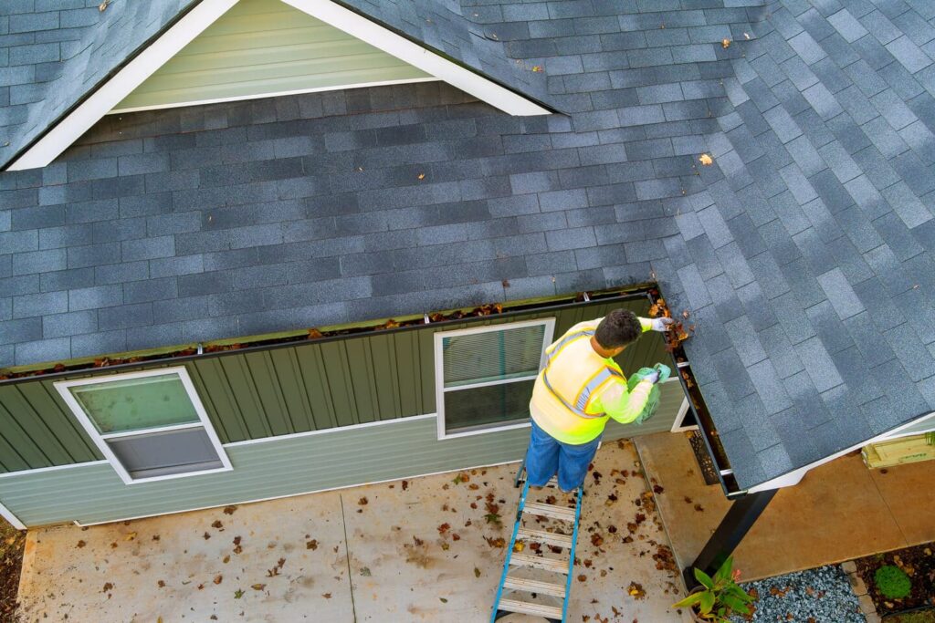 Person Cleaning Home Gutters in Autumn Season