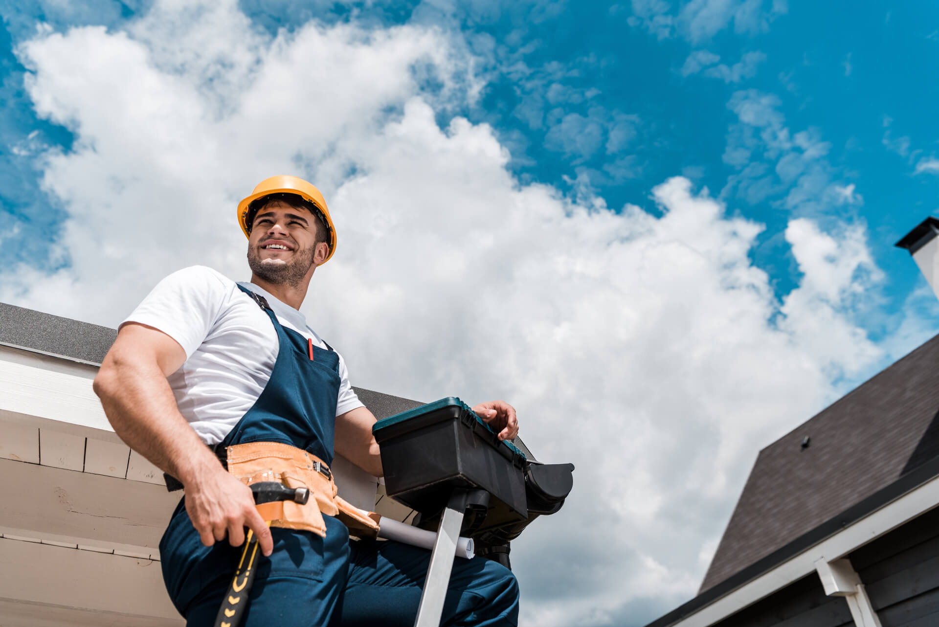 Low angle view of happy repairman in helmet holding hammer and toolbox